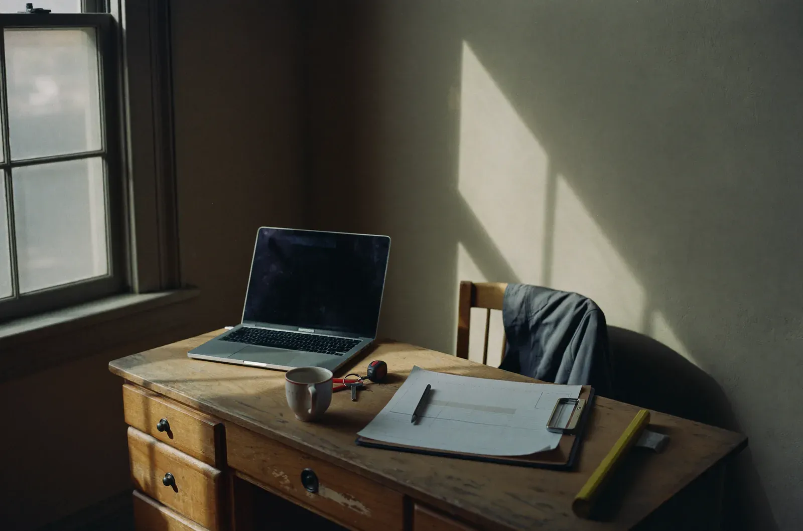 A job sheet, van keys and a mug on a worn desk in late afternoon light.