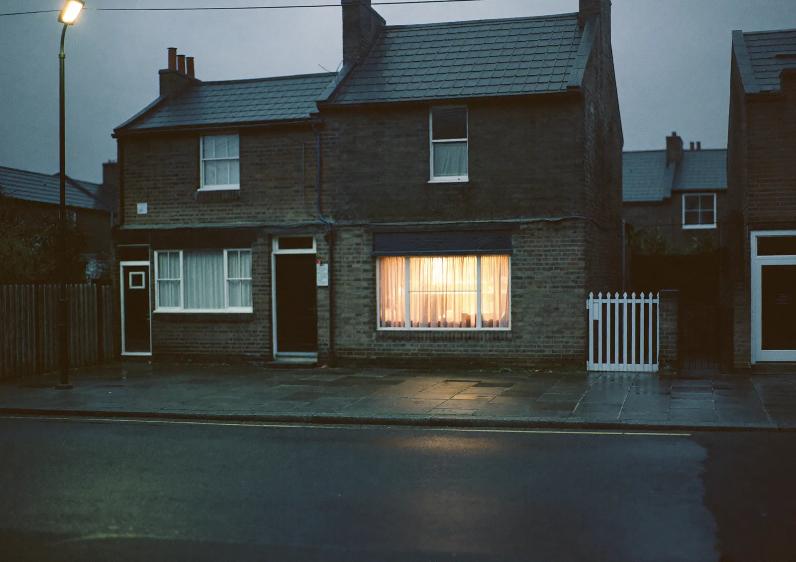 A terraced street at dusk with one front-room window lit
